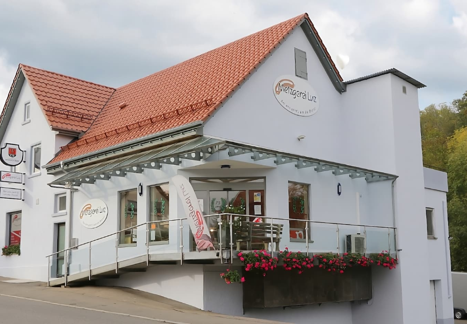 Außenansicht der Metzgerei und Gaststätte Luz in Reutlingen-Bronnweiler mit Glasvordach, Terrasse und roten Geranien
